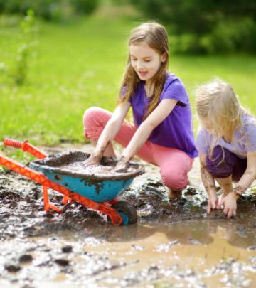 Two little girls playing in a large wet mud puddle on sunny summer day.