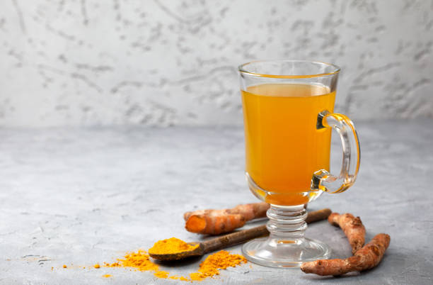 Turmeric tea in the glass with turmeric sticks and powder on the surface. 