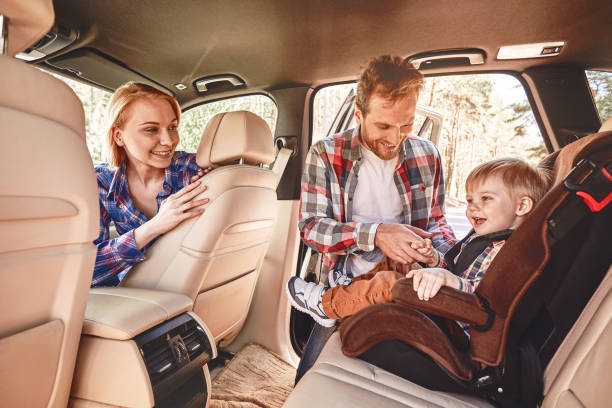 Parents trying to entertain their baby boy that sitting in a car in safety chair. 