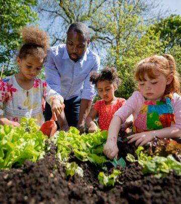 A low angle view of a teacher and three of his female pupils planting seedlings in a raised bed in the school garden in a school in Hexham in the North East of England. All three girls are using small gardening equipment to help plant.