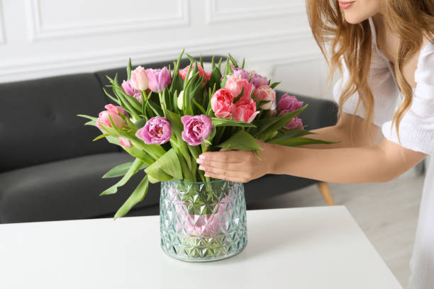 Woman putting bouquet of beautiful tulips in vase on white table indoors, closeup