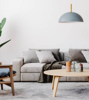 Modern living room setup with classic parquet floor. Furnished with light gray sofa, blue arm chair with wooden frame, modern blue ceiling lamp, wooden coffee table and gray carpet.