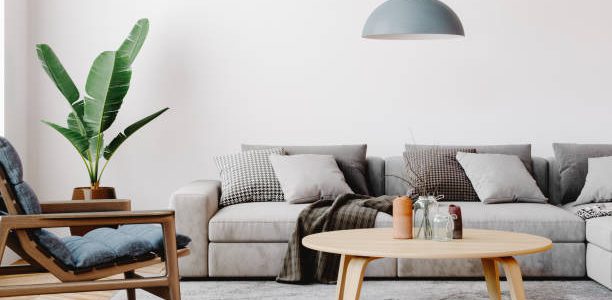 Modern living room setup with classic parquet floor. Furnished with light gray sofa, blue arm chair with wooden frame, modern blue ceiling lamp, wooden coffee table and gray carpet.