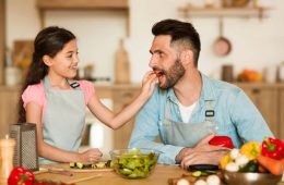 a cheerful young girl gives slice of fresh tomato to her delighted father during fun and interactive healthy cooking session