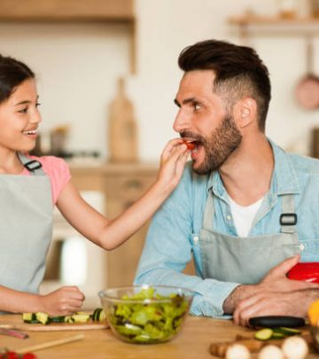 a cheerful young girl gives slice of fresh tomato to her delighted father during fun and interactive healthy cooking session