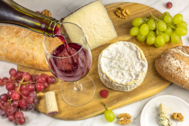 Red wine poured into a glass at a tasting, with various types of cheeses, bread, and grapes. Selective focus