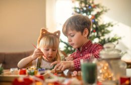 Children paint wooden toys near Christmas tree at home