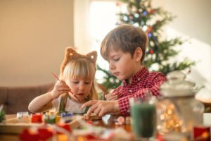 Children paint wooden toys near Christmas tree at home