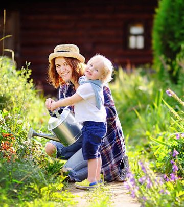 Cute toddler boy and his young mother watering plants in the garden at summer sunny day