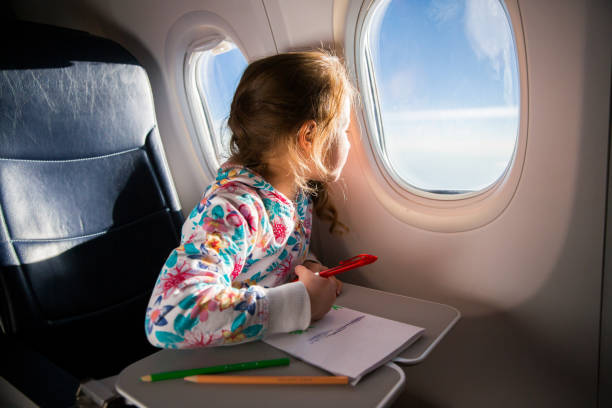 Child drawing picture with crayons in airplane. Little girl occupied while flying in aircraft. Travel with family and kids. Blue sky and sun outside the window