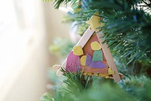 a paper and popsicle stick nativity scene made by my child hanging on a Christmas tree