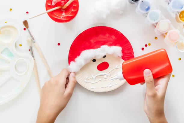 The child glues the parts Santa made from paper plate. Handmade. Project of children's creativity, handicrafts, crafts for kids. DIY. Step by step