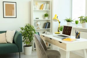 Cozy workspace with modern laptop on white wooden desk and comfortable chair at home