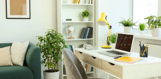 Cozy workspace with modern laptop on white wooden desk and comfortable chair at home