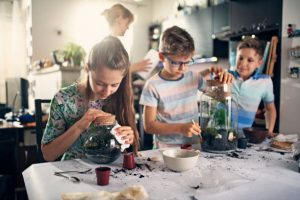 Kids having fun creating bottle gardens at home. They are potting little plants inside bottles to create miniature living eco-systems and beautiful home decoration. Nikon D850