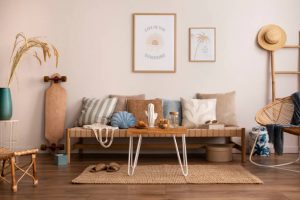 Sunny and bright space of living room with stylish sofa, pillows, coffee table, mock up poster frames, decorations, furnitures and personal accessories. Cozy home decor. Template. Summer vibe.